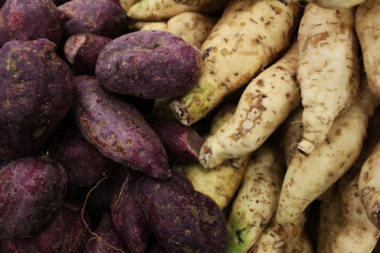 A vibrant display of purple and white sweet potatoes and radishes piled together.